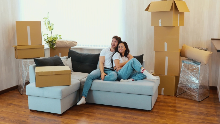 Young couple move into new apartment. Slow motion of man and woman sitting on couch and have fun together. Guy pointing forward and look at his girlfriend. | Shutterstock HD Video #1053214772