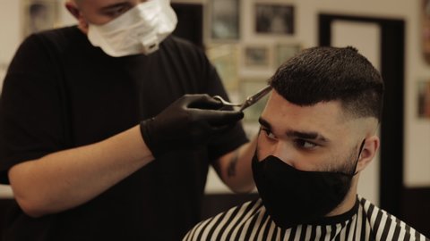 Men's haircut and hair styling in a barbershop, beauty salon. Haircut in quarantine. Client and barber in virus masks.