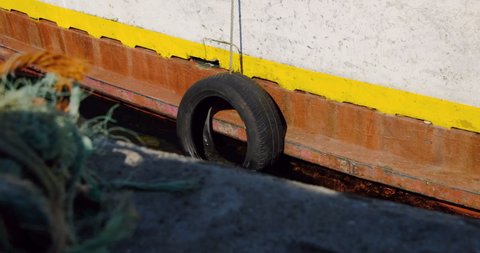 Povoa de Varzim, Portugal - May 25 2020: Old tyre hanging from hull of old fishing boat floating in the dock