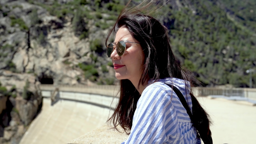 beautiful asian young girl backpacker relying leaning on railing of bridge enjoy wind blowing hair on sunny cool day. curiously woman looking down water river o shaughnessy dam with smoke hot spring