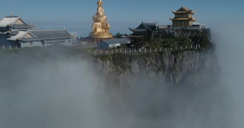 Camera rise up from the mist view of the Jinding of Emei mountain in the morning by the cliff at the summit shining golden buddha statue the UNESCO World Heritage site drone footage