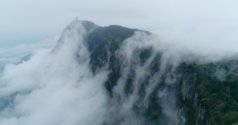 Amazing World Heritage site aerial view of mist flowing by the cliff with pine tree forest growing on the mountain summit with Chinese Traditional Architecture at Jinding Emei above the sea of clouds 