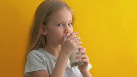 girl drinks milk on a yellow background. little girl with blonde hair and blue eyed, drinks milk. People sincere emotions on yellow background, lifestyle concept