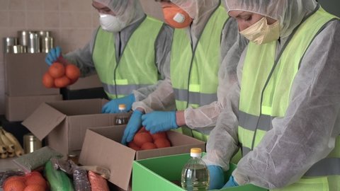 Food For The Poor, Feeding the Hungry, Charity organization. Food donation during Coronavirus COVID-19. Hispanic volunteers, social worker in protective suits gloves and masks collect a grocery boxes