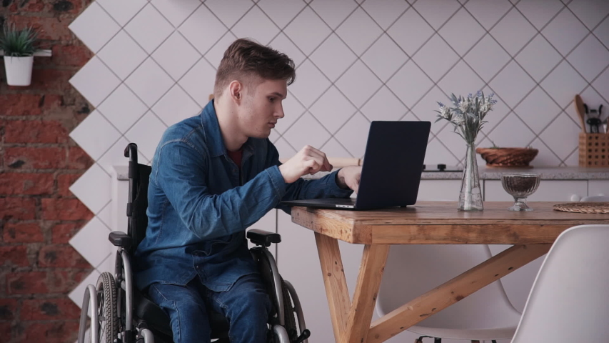 Man in wheelchair working with laptop at home. Adult disabled male working studying on laptop and checking news mail. sitting in modern kitchen interior. concept computer Royalty-Free Stock Footage #1053229514