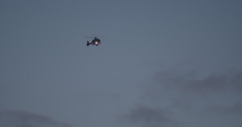 Police helicopter flying in front of dark sky, light attached to search for a person.