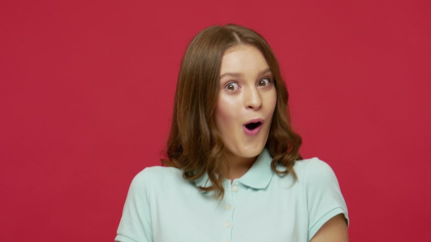 Closeup of surprised excited young woman in t-shirt opening her mouth in amazement, shouting Wow, astonished by sudden shocking news, expressing disbelief. studio shot isolated on red background | Shutterstock HD Video #1053232133