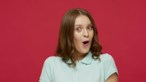 Closeup of surprised excited young woman in t-shirt opening her mouth in amazement, shouting Wow, astonished by sudden shocking news, expressing disbelief. studio shot isolated on red background