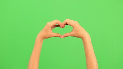Closeup view of female hand making heart shape gesture isolated on green screen chromakey background. Person forms a heart shape using their fingers. Two handed gestures. Chromakey. Green Screen.
