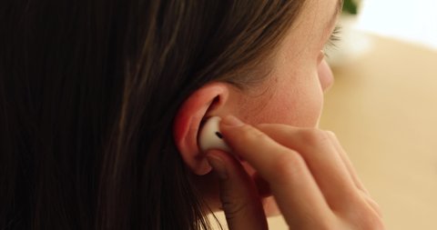 Woman inserts a wireless white earphone into her ear close-up