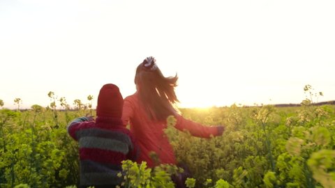 Cute children run holding hands in a yellow, blooming field in the countryside at sunset. The concept of childhood, carelessness and joy, shooting from the back