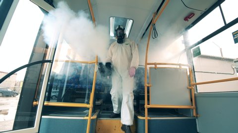 Sanitation worker disinfects bus with a sprayer.