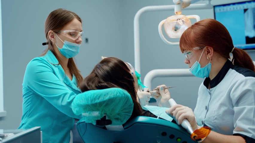 Dentist and assistant treating teeth to female patient. Stomatologist speaking to a client in the dental office. Tooth treatment. | Shutterstock HD Video #1053243332