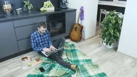 Young male freelancer typing on laptop computer and working from home workplace during self isolation and quarantine. Man works on notebook from home at cozy living room