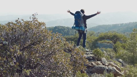 Backpacker climbing on top of mountain and raising hands celebrating great achievement and enjoying beautiful nature view. Hiker standing on top of hill