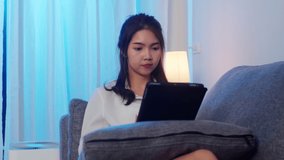 Asian businesswoman using tablet talk to colleagues about plan in video call while working from home at living room at night. Self-isolation, social distancing, quarantine for coronavirus prevention.