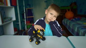 Sad child dreams of a puppy. A boy sits at a table with a toy dog. Kid dreams of making friends. A game with a robot dog. An upset child looks out the window during quarantine. Loneliness. Lockdown. - Powered by Shutterstock - Get 15% off with code: PIKWIZARD15