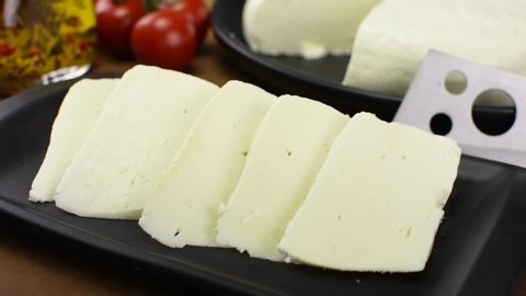  Pouring olive oil in slices of buffalo fresh cheese made in Serra da Canastra, in a platter in wood background