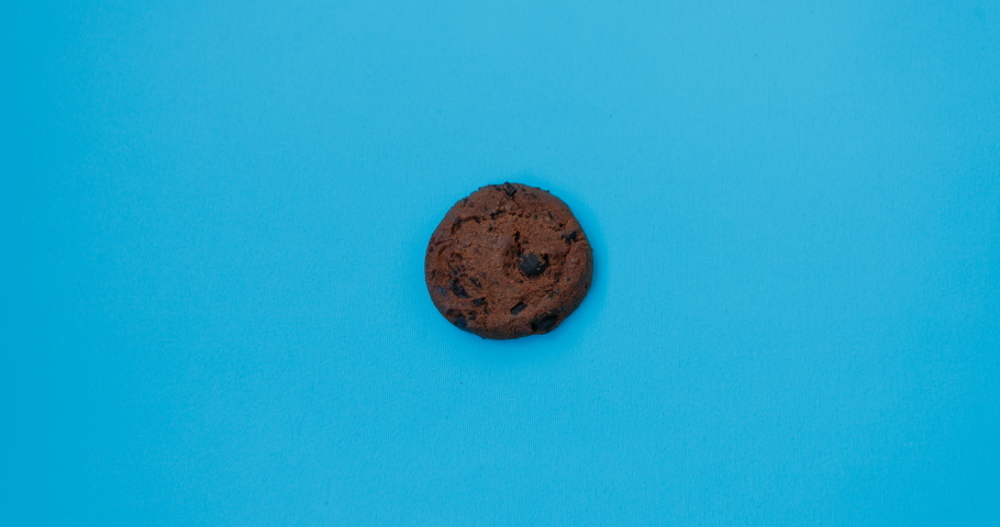 Moving and disappearing chocolate chip cookie on blue background, stop motion. 4K. Abstract colorful animation. Food, eating concept | Shutterstock HD Video #1053257120