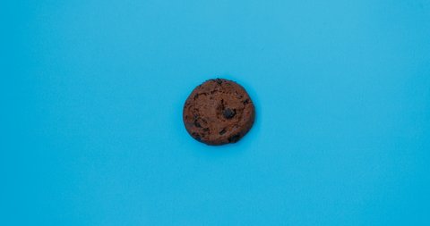 Moving and disappearing chocolate chip cookie on blue background, stop motion. 4K. Abstract colorful animation. Food, eating concept