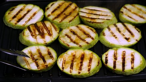Zucchini fried on the grill.With tongs turns the zucchini in the electric grill.Vegetarian dish.Hands turns the vegetables on the grill.Cooking vegetables without oil.Non-stick coating.Close-up.