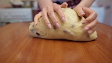 female hands knead soft dough with raisins on a wooden table in the kitchen, closeup slow motion. cooking desserts in the oven at home.