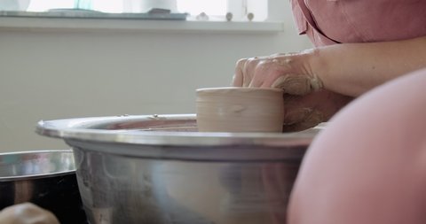 Female potter sitting and makes a cup on the pottery wheel. Woman making ceramic item. Pottery working, handmade and creative skills