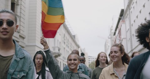 Happy young people with rainbow flag at gay parade. Group of men and women participating in gay pride march in the city.
