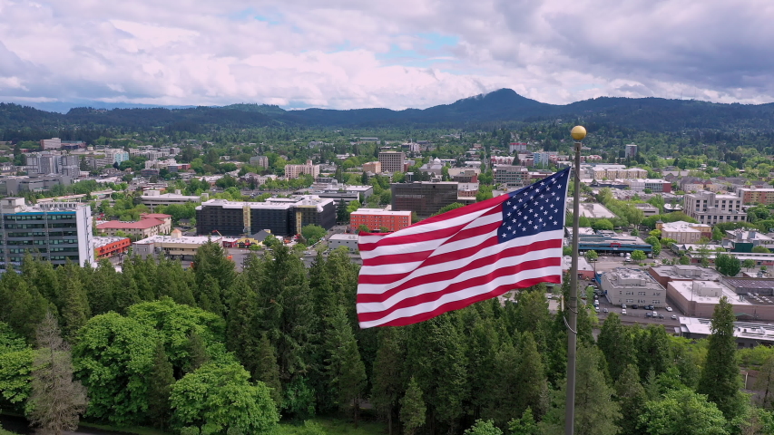 American Flag waving in aerial view of Eugene Oregon slowly flying around the flag.