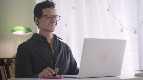 A young male businessman is celebrating the success of target completion with his team members, employees, coworkers over a video call on the laptop while sitting and working from home during lockdown