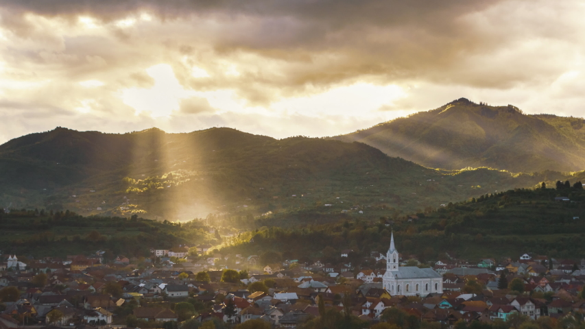 Epic rays and beams of sunlight through the clouds and the rain, rural landscape with church and buildings under the mountains 4k timelapse | Shutterstock HD Video #1053271415