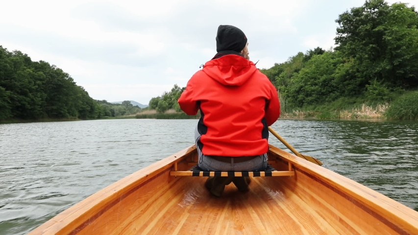Rear view of man paddling canoe on cloudy day, slow motion