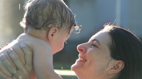 Mother caring and kissing infant toddler child baby at the swimming pool in slow-motion