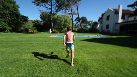 Child boy running, sprinting in home backyard garden and doing a back flip into swimming pool water.