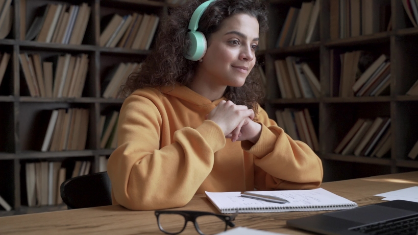 Hispanic teen girl school pupil college student wear headphones learning online with teacher tutor waving hand using video conference call by webcam on laptop computer. Videoconference education. Royalty-Free Stock Footage #1053275738
