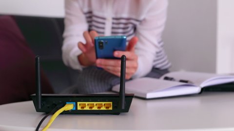 Closeup of a wifi router and a redhead woman using smartphone on living room at home office. Shut and restart to connect the wifi router
