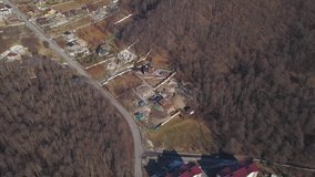 Large housing development in the countryside area. Clip. Flying over the village and construction site with unbuilt houses surrounded by bald tree forest.