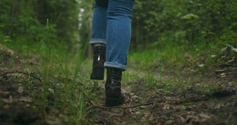 Close up of women legs hiking steep terrain in slow motion. Feet in Hiking Boots Walking on Autumn Road. woman feet tracking on fall day outdoors, walking through woodland
