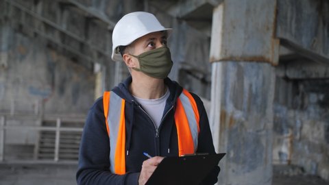 Engineer in the construction helmet and antiviral protective mask inspects a building or object reconstruction. A gradual exit from the quarantine mode.