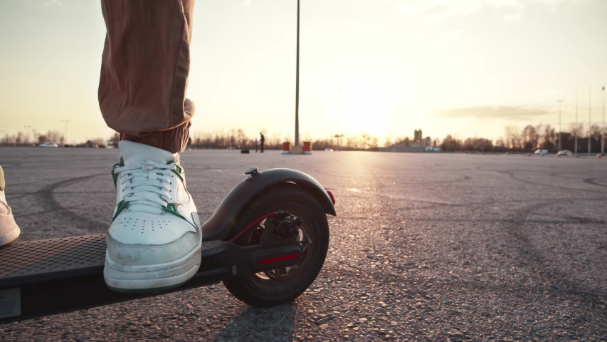 Shot on legs young man in white sneakers ride on electric mobile scooter outside parking space at sunset. Beautiful scenery, nature. Eco-friendly transportation. Royalty-Free Stock Footage #1053283751