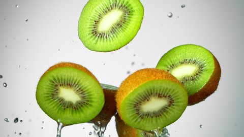 Super Slow Motion Shot of Flying Kiwi Slices and Splashing Water on Grey Gradient Background at 1000fps.