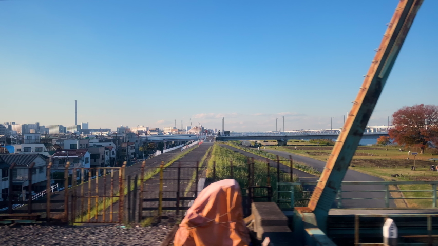 POV Side Shot of looking out from Narita Express crossing bridge in Tokyo, Japan during the day in slow motion.