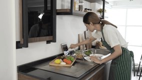 Woman prepare piece of bread and lettuce into salad plate follow cooking online video clip via tablet.