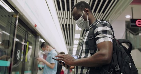 Side view of one black man wear mask in the subway using mobile phone passengers in the train all with mask during pandemic of coronavirus Covid-19