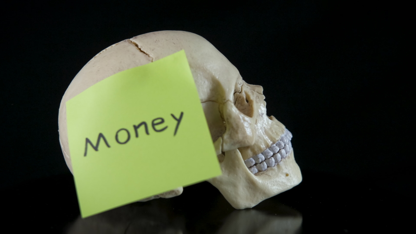 Money under risk. A view of a human skull with the sticker with the word money writing on it on the black bakcground.