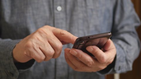 A Man's Hands Using A Smartphone, Close Up. Elderly Man Holding Mobile Phone, Writes Text. A Man In A Gray Shirt..