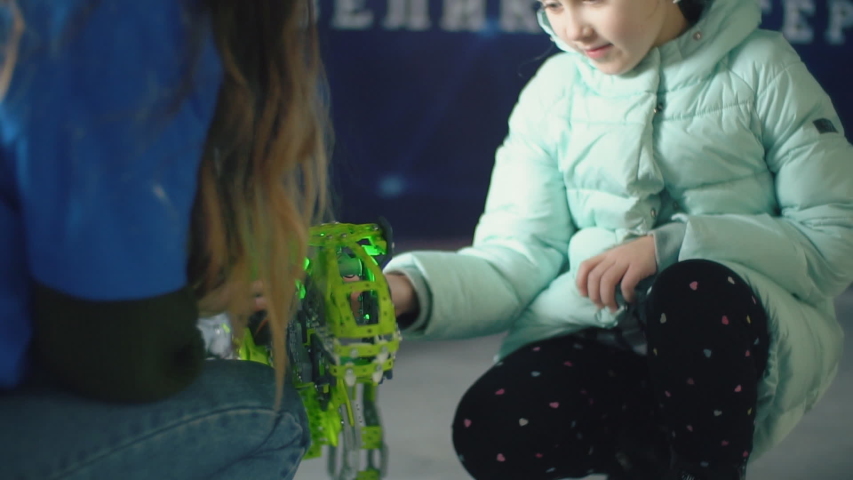 girl stroking the head of a green dinosaur robot