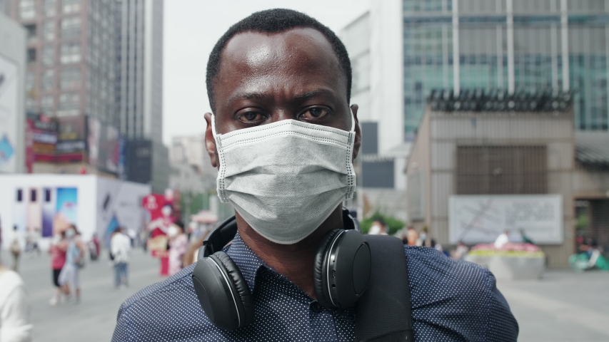 Close up of one black African man wear face mask looking at camera at urban city street background coronavirus Covid-19 pandemic outbreak with crowd people wear mask walking at background Royalty-Free Stock Footage #1053303800