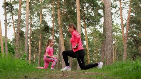 Young sporty mother and little cute daughter doing fitness training exercise together in a forest.