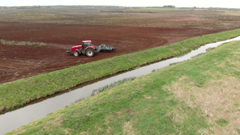 Aerial: a farmer on a modern tractor cultivates farmland with a disc harrow near a small reclamation river. Concept of agribusiness. Problem of water pollution and siltation by agricultural production